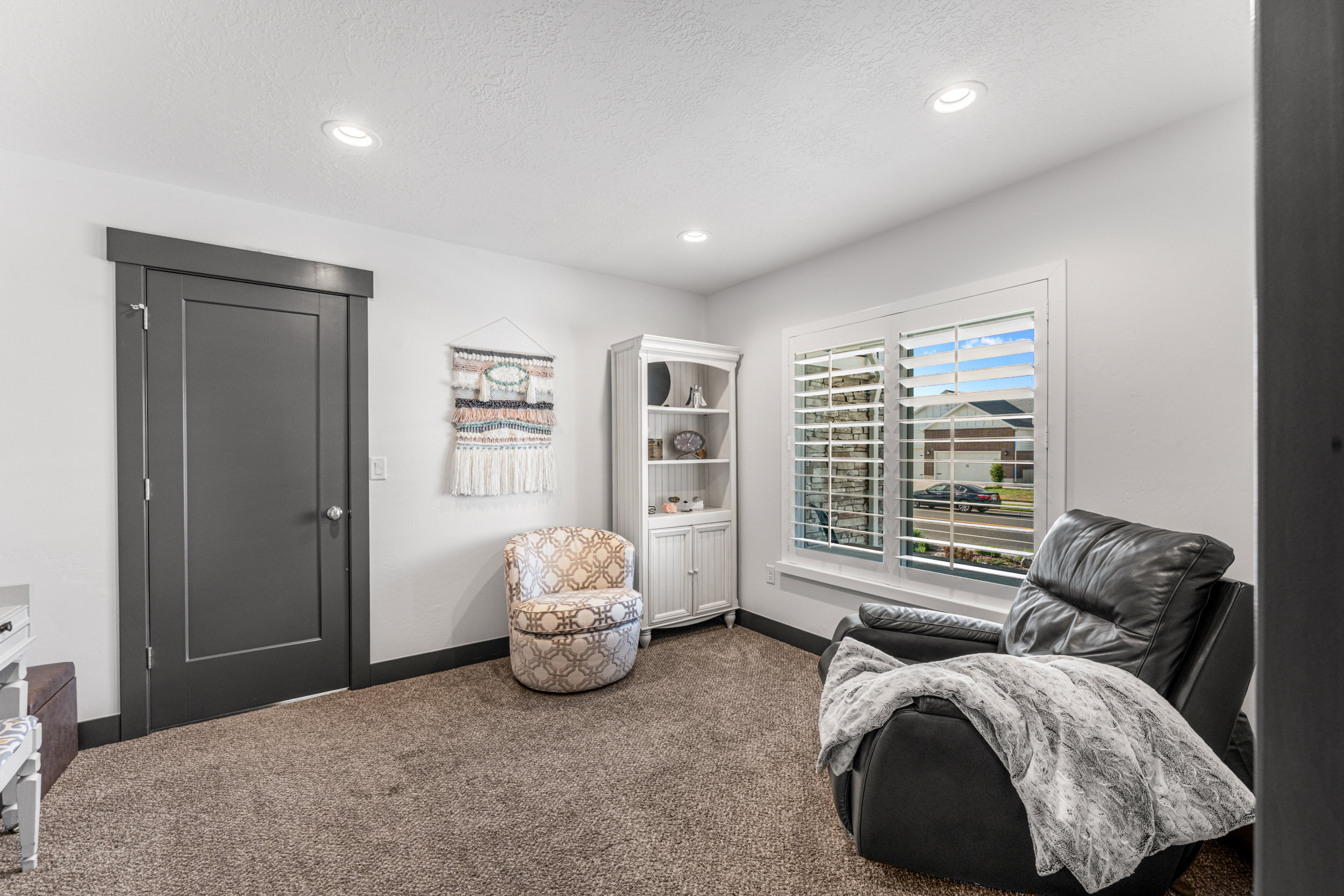Recessed lighting illuminates the room, featuring a window with white plantation shutters and a dark gray door with coordinating trim and baseboard