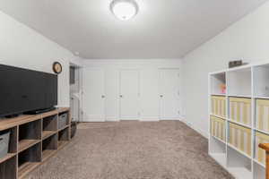 Spacious room featuring neutral carpet flooring, white walls, multiple white panel doors, and a flush-mount ceiling light fixture