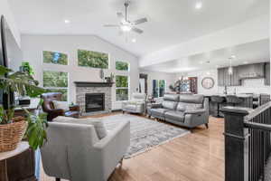 Vaulted living room with a stone-clad fireplace and wood-finish flooring