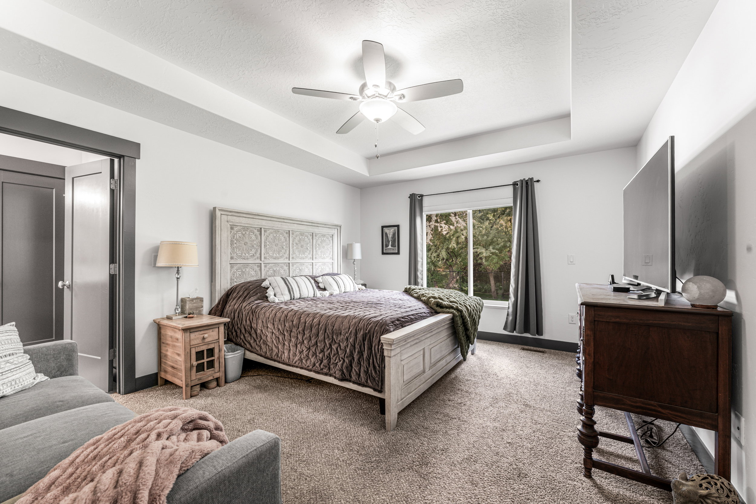 Spacious room featuring a decorative headboard, tray ceiling, recessed lighting, and a ceiling fan