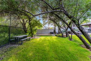 Expansive green space featuring mature trees, a picnic table, and a chain-link fence
