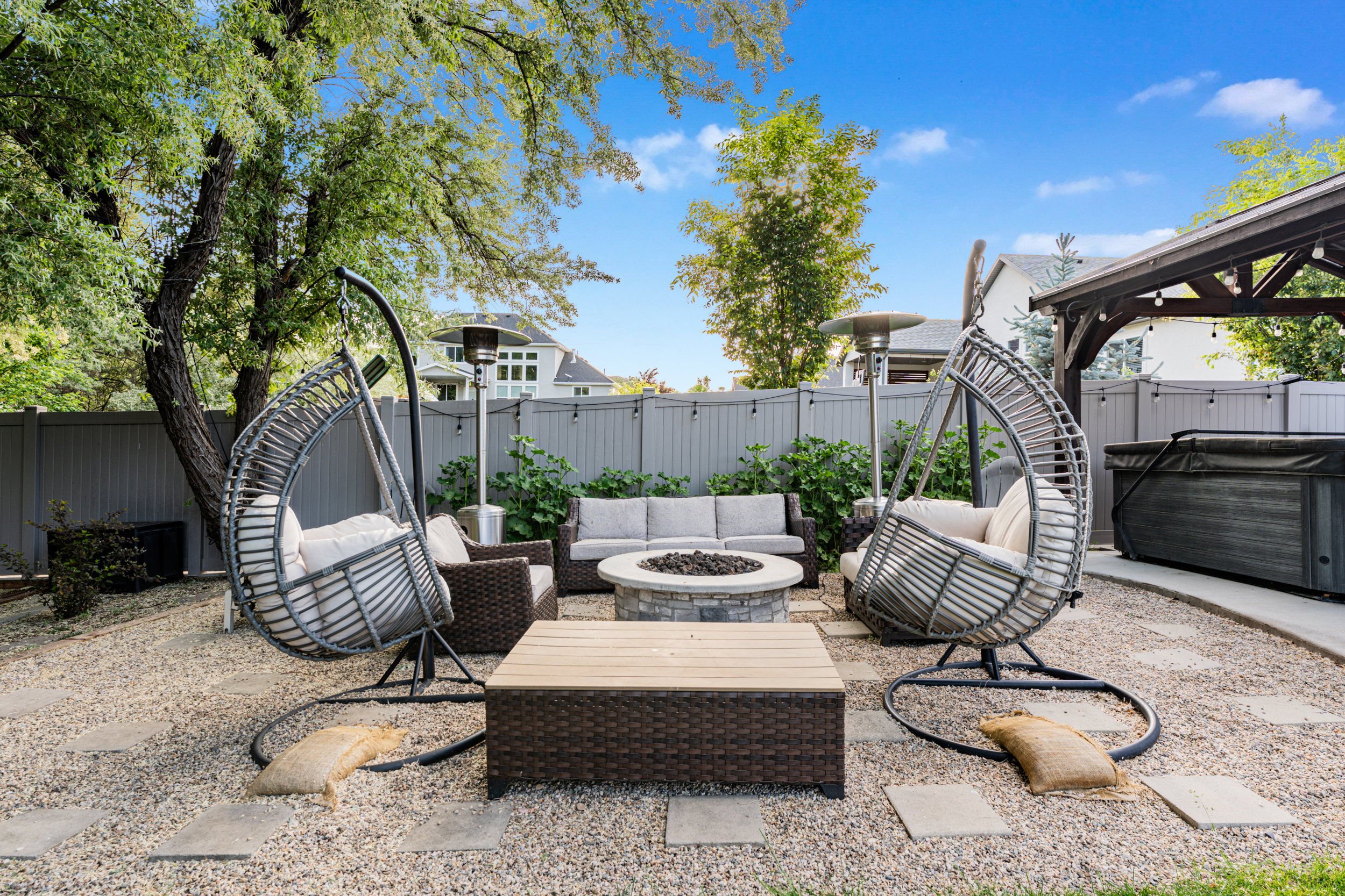 Landscaped backyard featuring a central fire pit, stone pavers, and a gravel surface