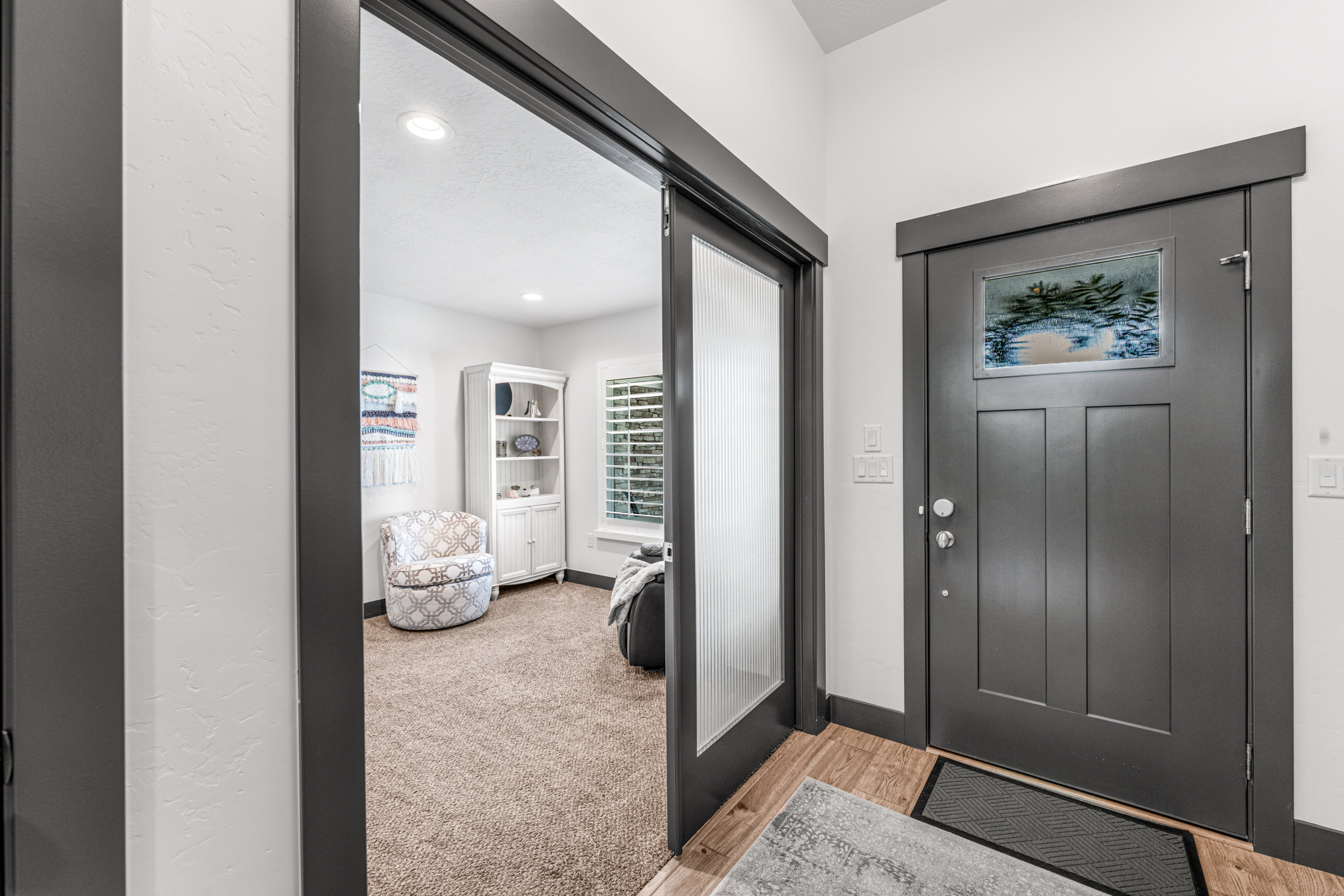 Entryway featuring a dark gray paneled door with decorative glass inlay, wood-finish flooring, and a pocket door with frosted glass paneling
