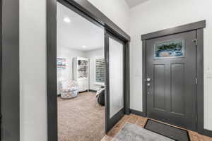 Entryway featuring a dark gray paneled door with decorative glass inlay, wood-finish flooring, and a pocket door with frosted glass paneling