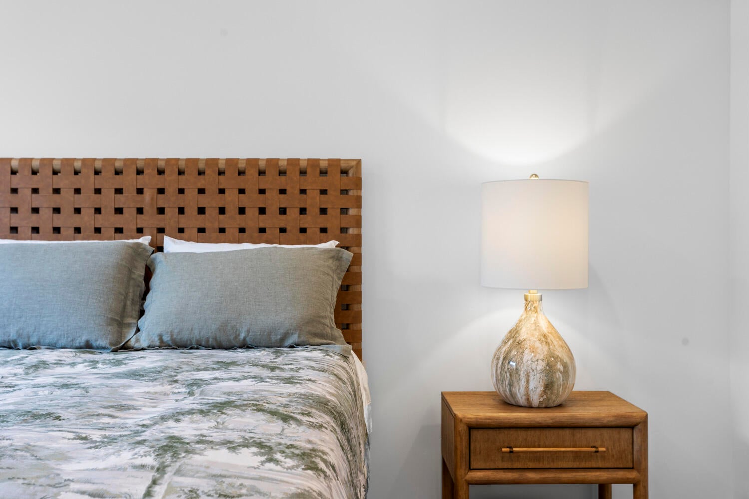 Woven leather-finish headboard accentuates this bedroom space, complemented by a wood-finish nightstand and contemporary lighting fixture