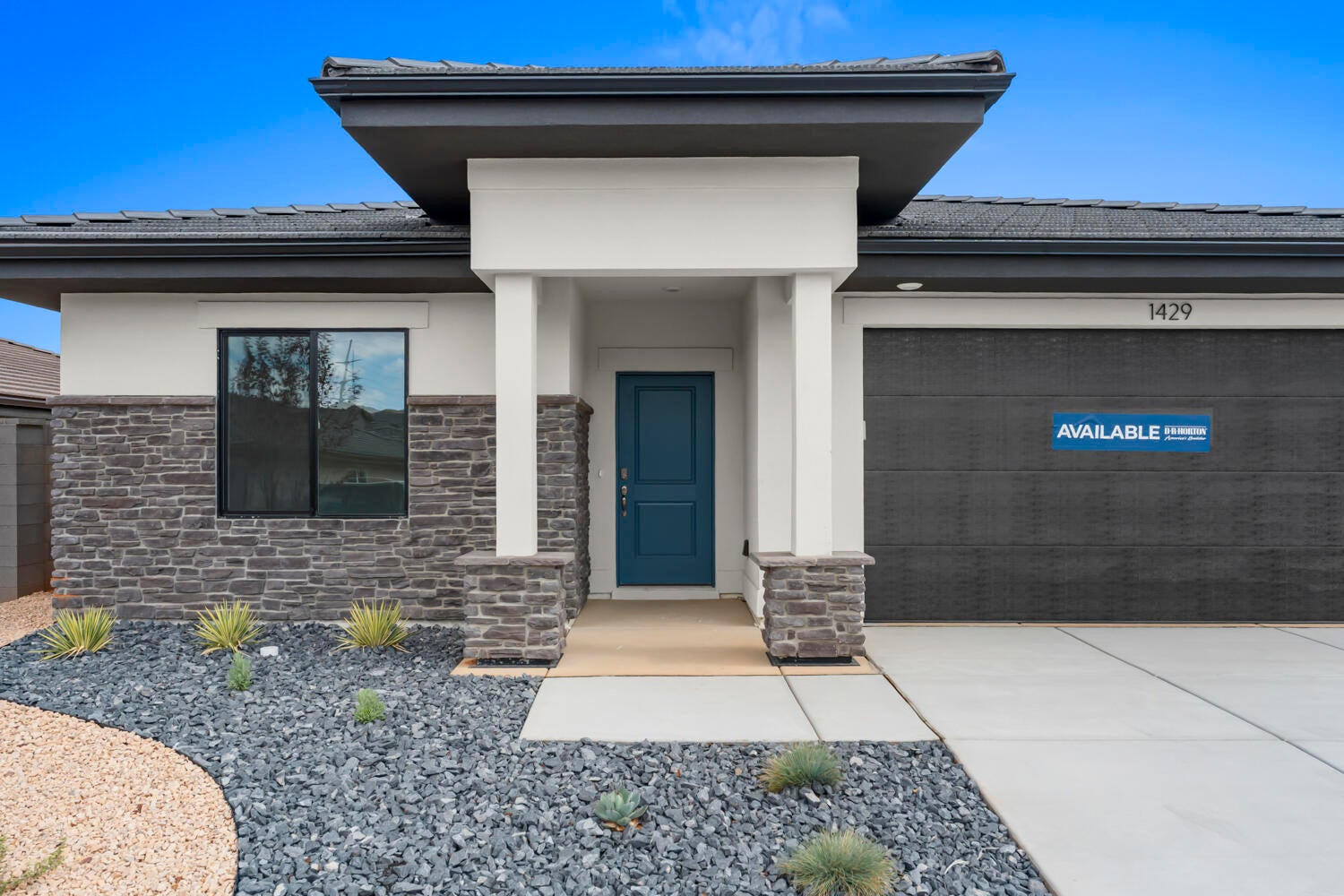 Modern exterior featuring a stone and stucco facade, a prominent teal entry door, a textured garage door, and a low-maintenance landscape design with decorative rock