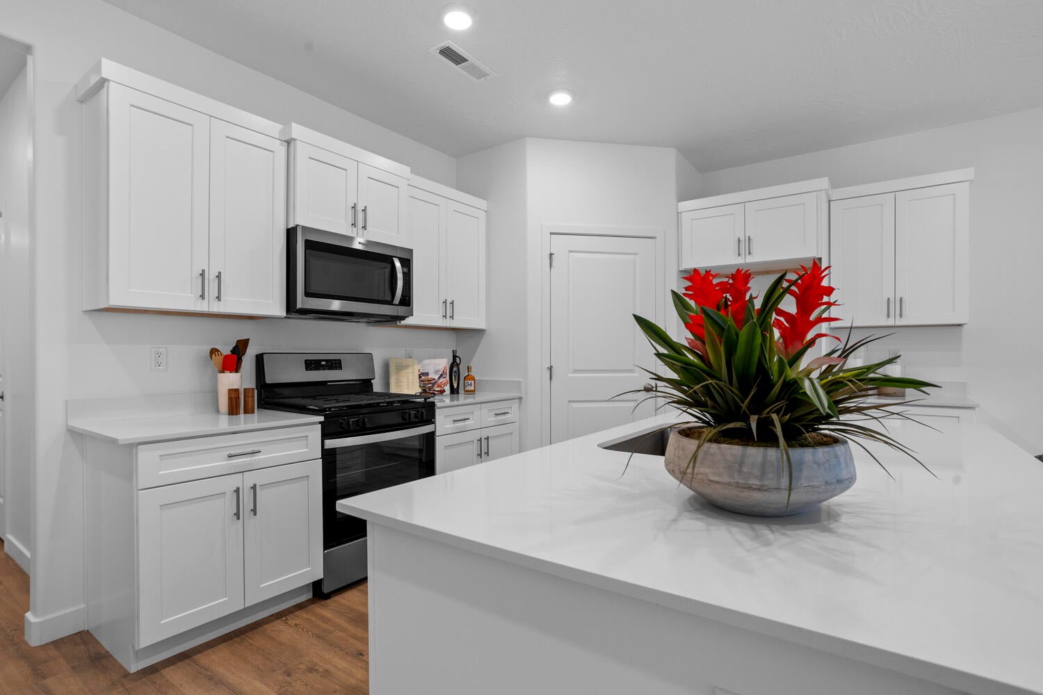 Modern kitchen featuring white shaker-style cabinetry, a stainless steel microwave, a built-in oven with a gas range, and light-colored countertops