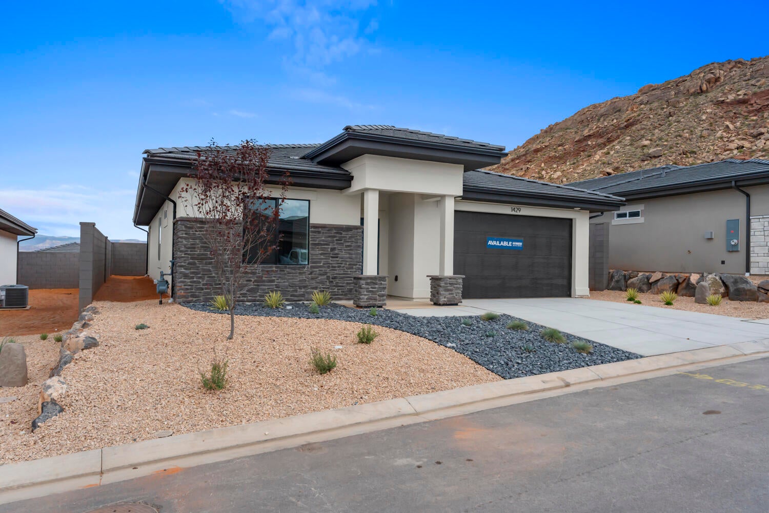 Contemporary single-story exterior featuring a dark gray tile roof, light stucco, and dark stacked stone accents