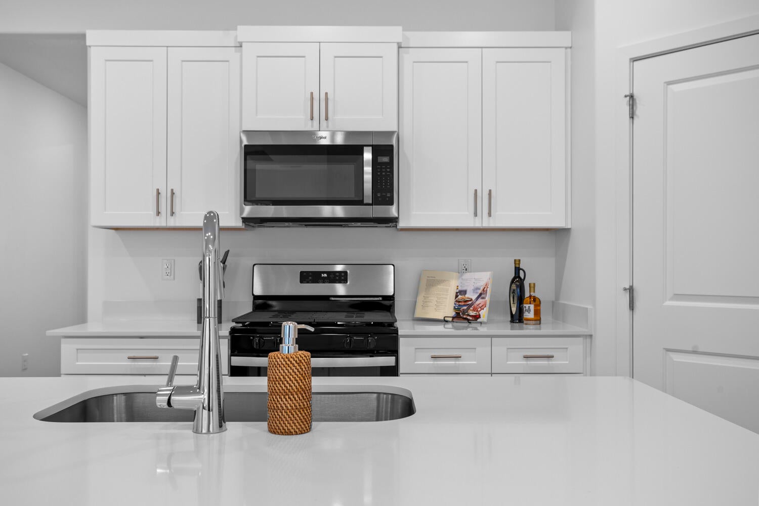 Kitchen featuring white shaker cabinetry, stainless steel appliances, light-toned countertops, an undermount sink, and a chrome faucet