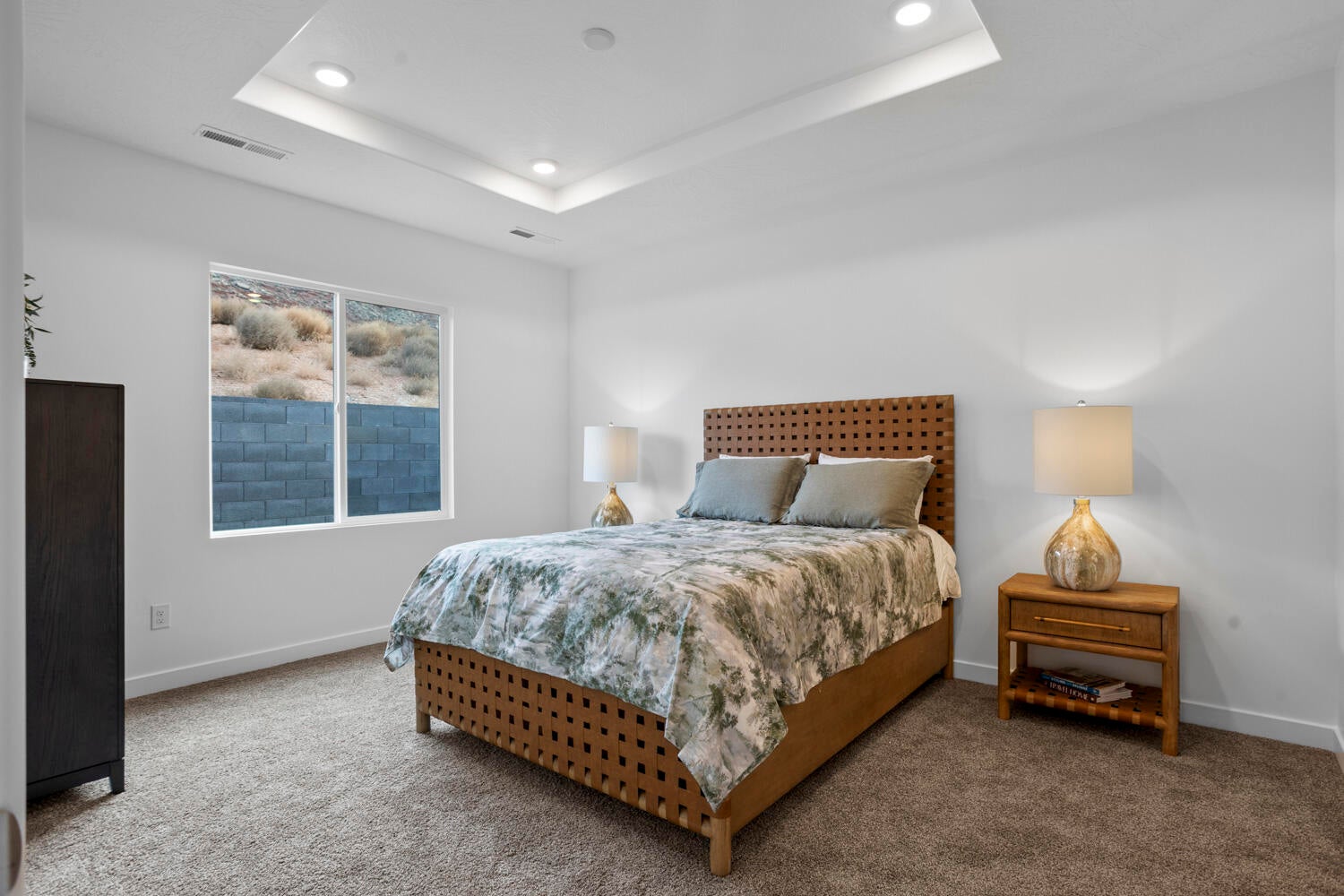 Recessed ceiling lighting, tray ceiling, and a large window with desert landscaping and a block wall
