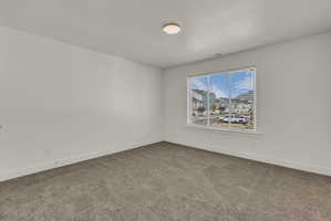 Spacious room featuring neutral carpeting, white painted walls, a large window with blinds, and an overhead flush-mount light fixture