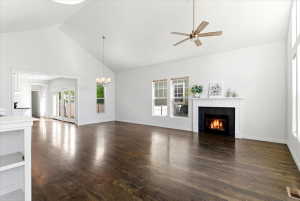 Spacious living room featuring vaulted ceilings, hardwood flooring, a fireplace with a white mantel and black tile surround, multiple windows, and a ceiling fan
