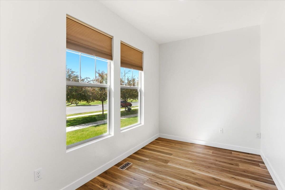 Room featuring two large windows with pleated blinds, wood-finish flooring, and white baseboards