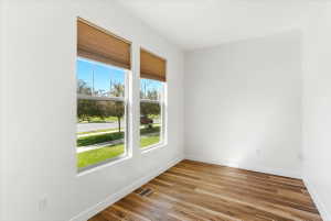 Room featuring two large windows with pleated blinds, wood-finish flooring, and white baseboards