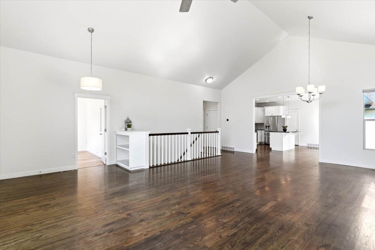 Spacious living area featuring vaulted ceilings, hardwood flooring, a contemporary chandelier, and a white balustrade with built-in shelving