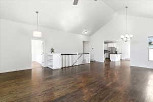 Spacious living area featuring vaulted ceilings, hardwood flooring, a contemporary chandelier, and a white balustrade with built-in shelving