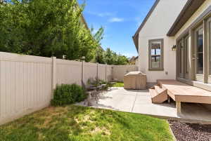 Outdoor patio space featuring a light-colored privacy fence, concrete patio, and a tiered wood-finish deck with steps