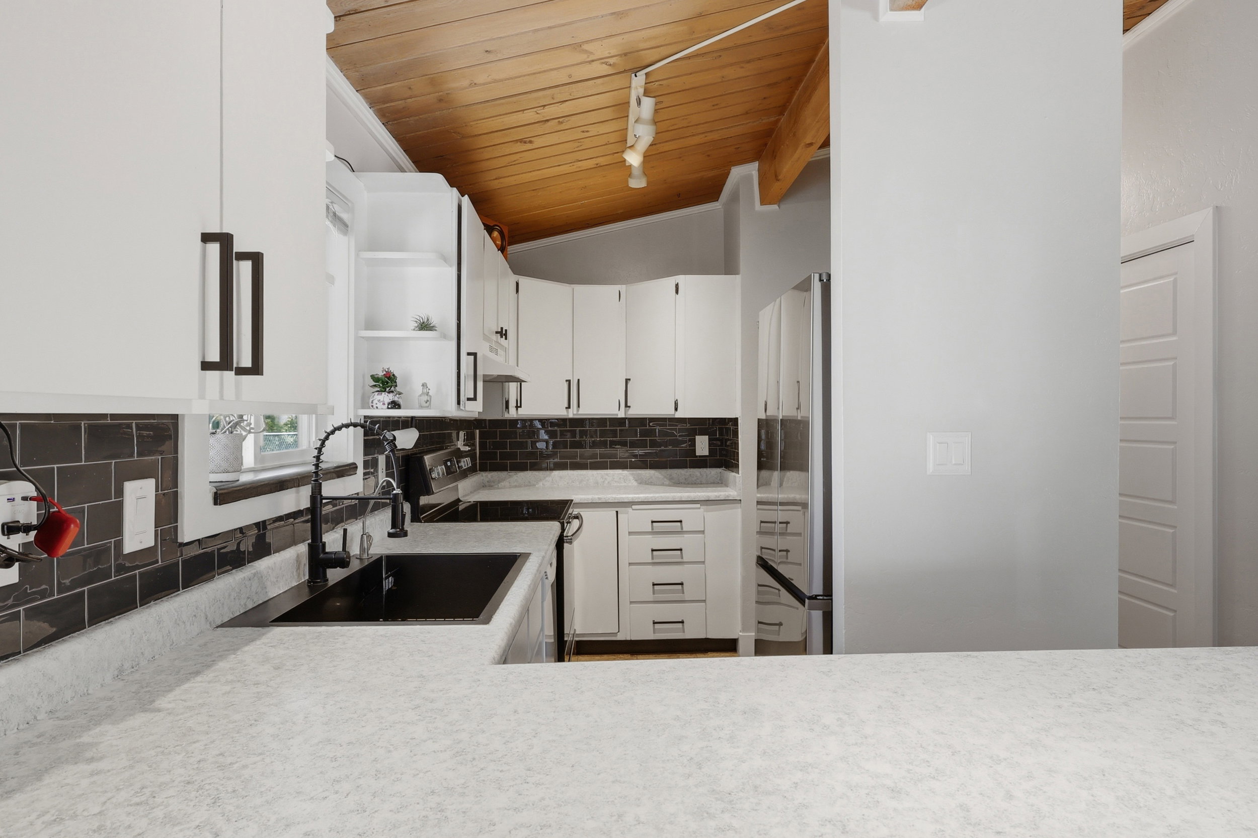 Modern kitchen featuring white cabinetry with dark pulls, dark subway tile backsplash, and light-colored countertops