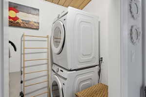 Dedicated laundry area featuring a stacked washer and dryer, wood-panel ceiling, and white walls