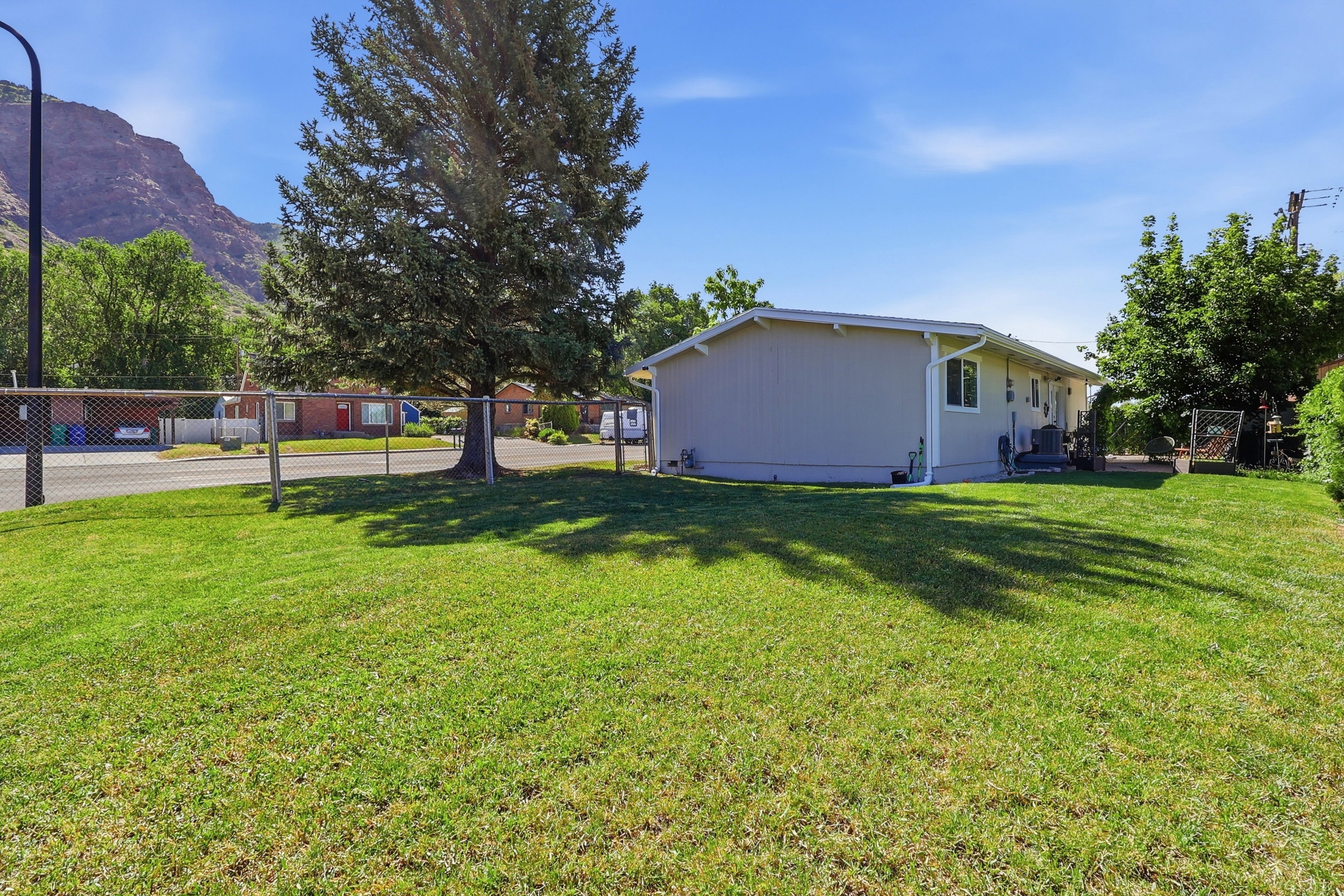 Expansive grass yard with chain-link fencing, mature trees, and a mountain backdrop