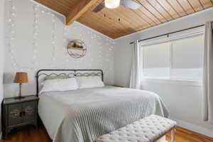 Bedroom featuring wood-finish flooring, a sloped wood-paneled ceiling with an exposed beam, and a ceiling fan with integrated lighting