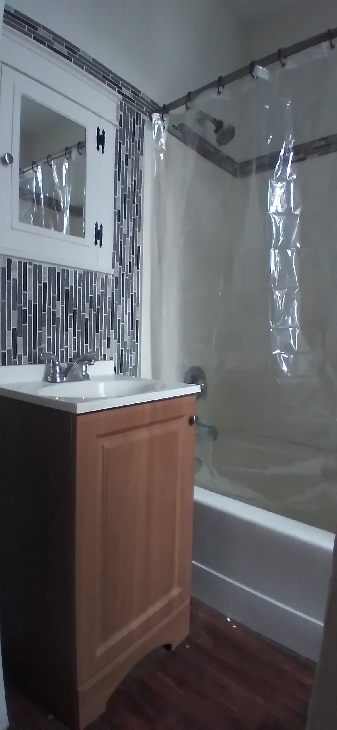 Bathroom featuring wood-finish flooring, a vanity with a white countertop and integrated sink, chrome faucet, a white medicine cabinet, and a tiled shower surround
