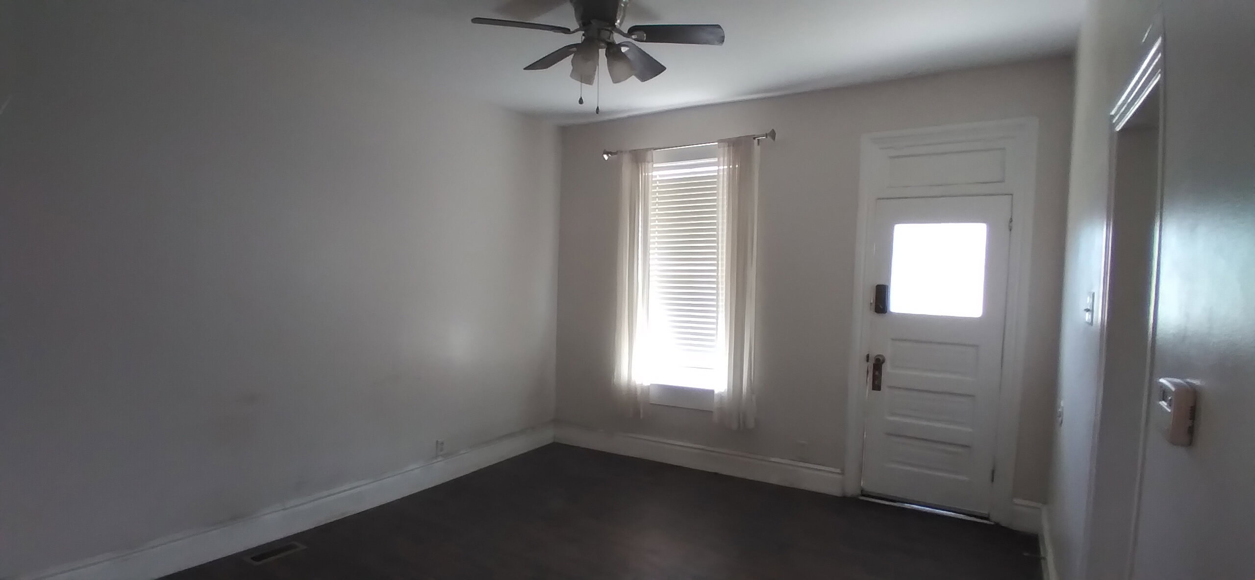 Room featuring dark wood-finish flooring, a ceiling fan, and a window with blinds