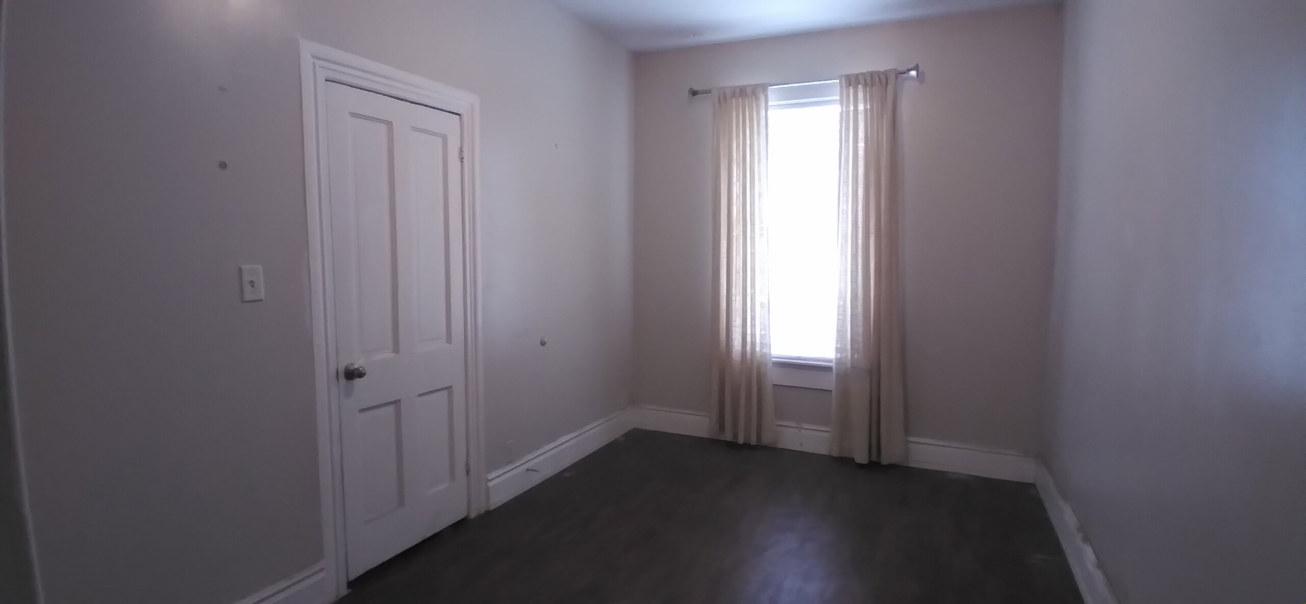 Room featuring wood-finish flooring, a two-panel door with white trim, and a window with natural light and drapes