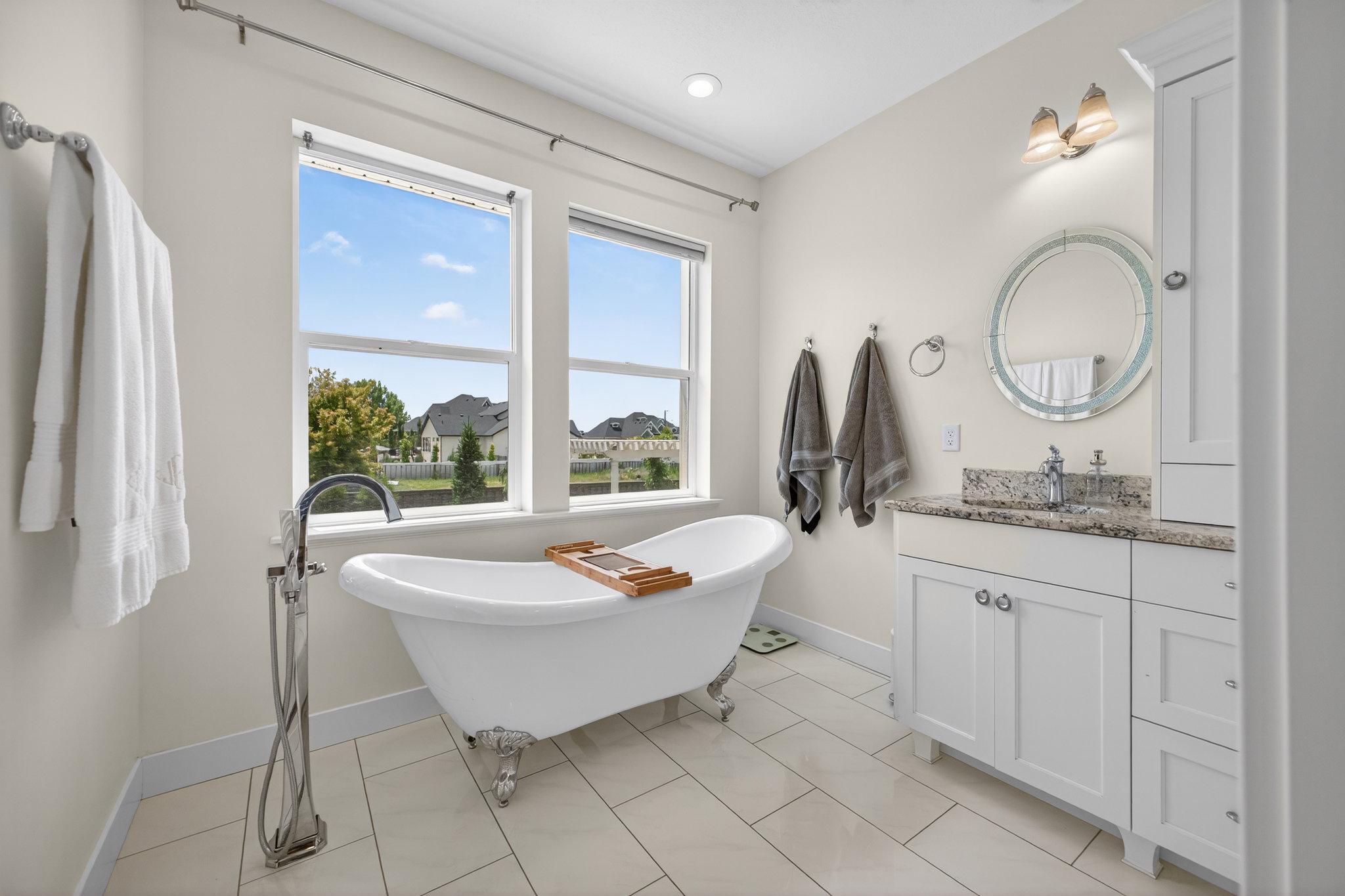 Freestanding clawfoot tub with a floor-mounted faucet, dual windows, and light-toned plank flooring