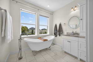Freestanding clawfoot tub with a floor-mounted faucet, dual windows, and light-toned plank flooring