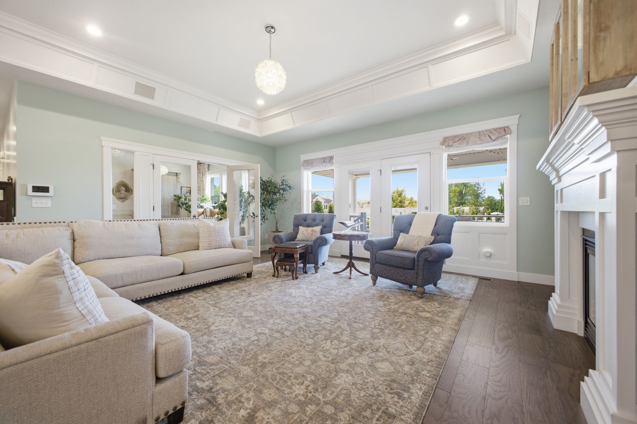 Spacious living area featuring coffered ceilings with recessed lighting, a decorative chandelier, a white mantel fireplace, and dark wood-finish flooring
