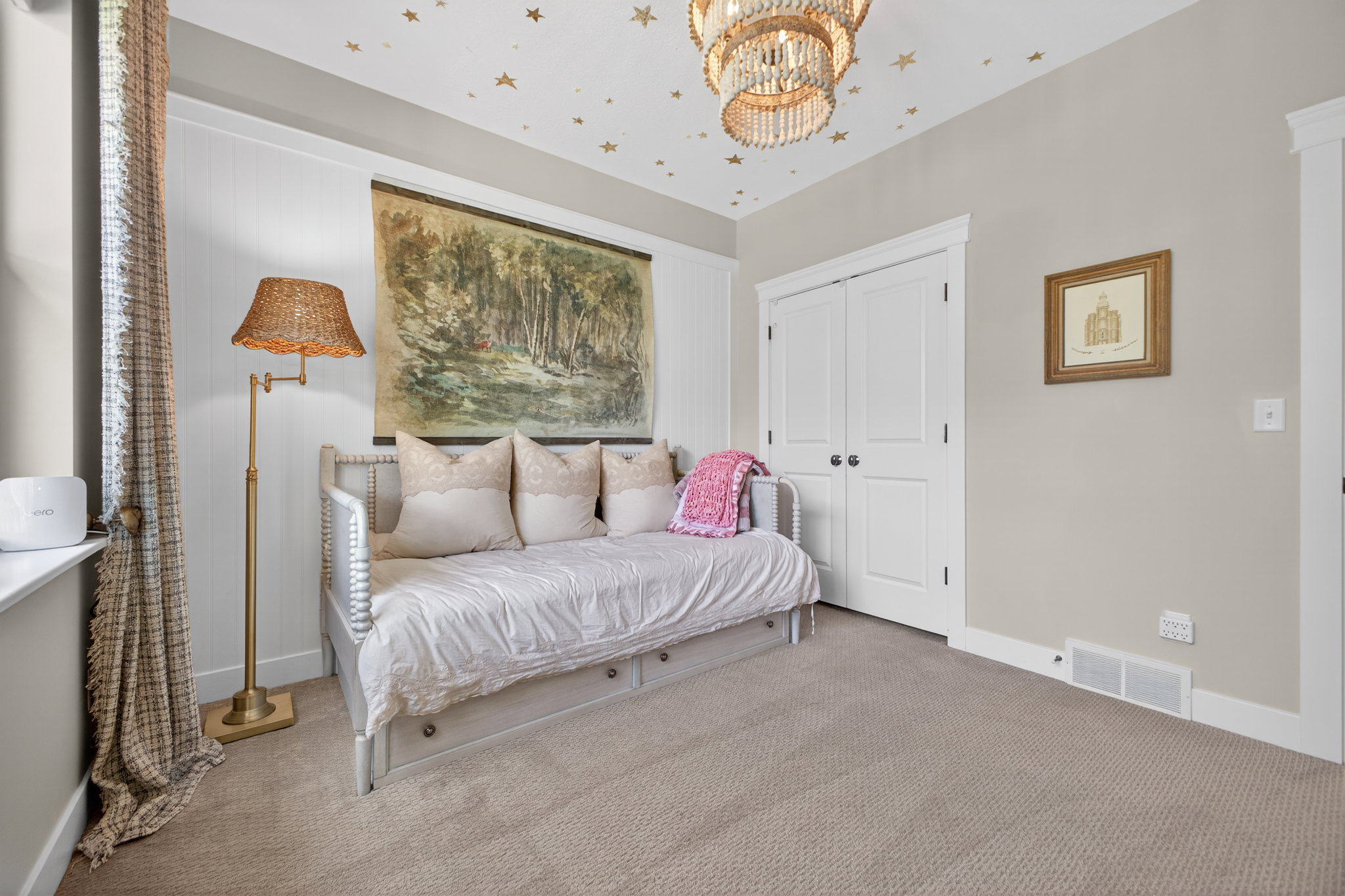 Carpeted room featuring a double-door closet with black hardware, a window with patterned curtains, and a decorative ceiling fixture