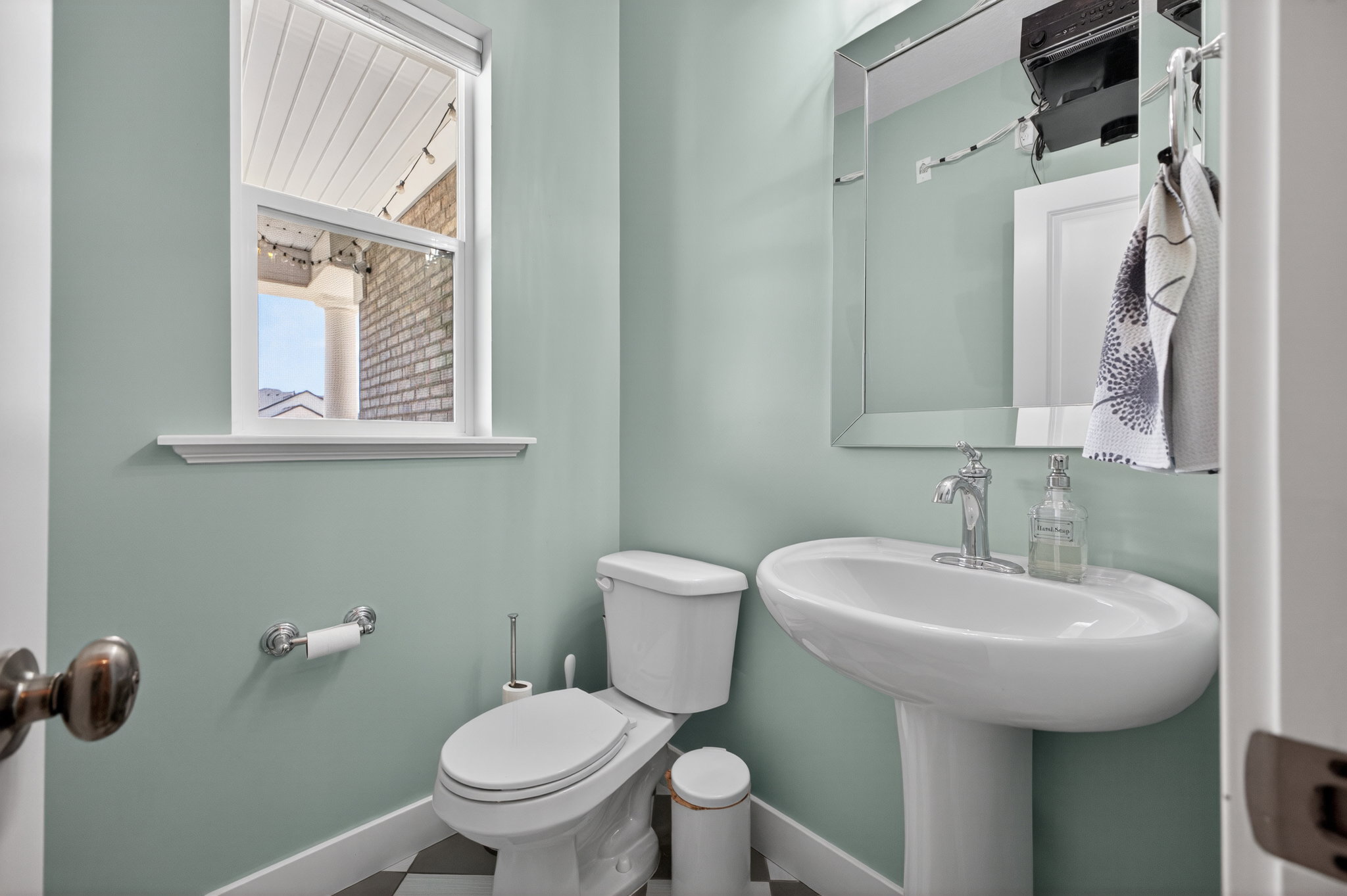 Pedestal sink with chrome faucet, white toilet, and window with a view of a brick exterior