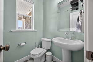 Pedestal sink with chrome faucet, white toilet, and window with a view of a brick exterior
