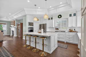 Gourmet kitchen featuring white cabinetry, stainless steel appliances, a large central island with seating, recessed lighting, and wood-finish flooring