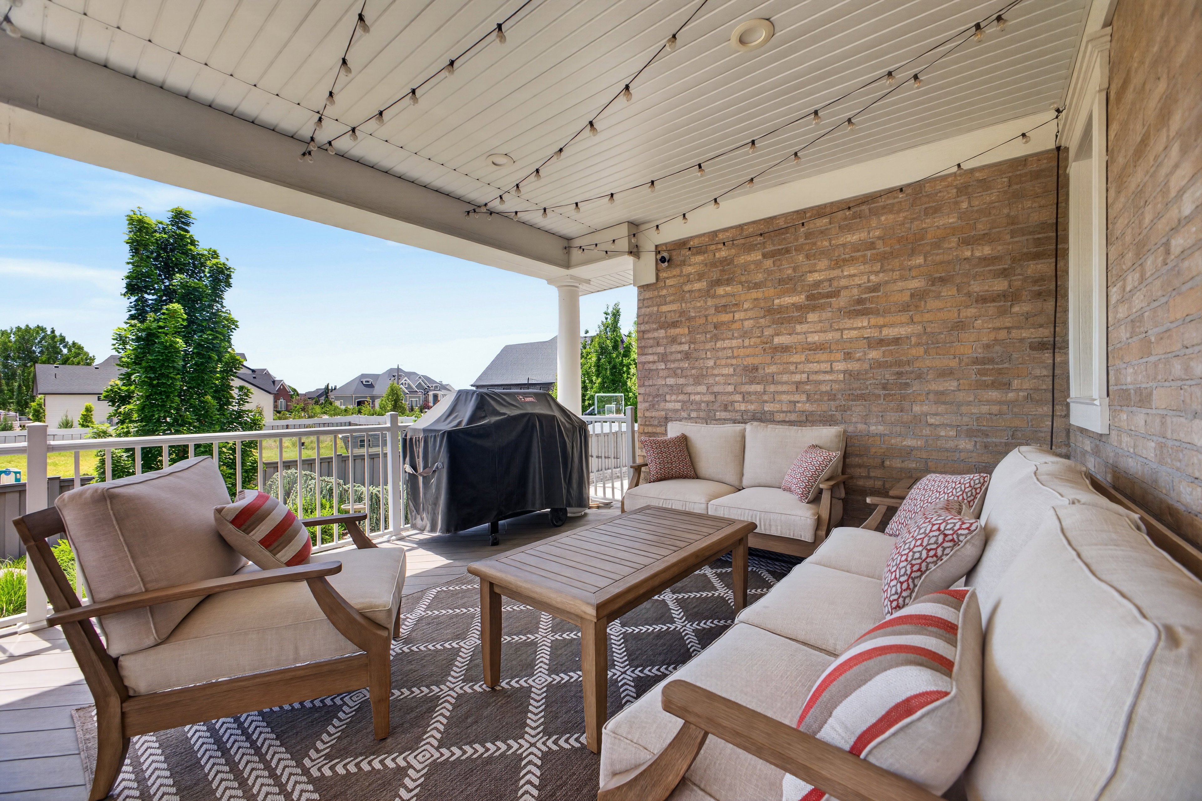 Expansive covered patio featuring a brick exterior wall, white railing, outdoor ceiling fan, and string lights