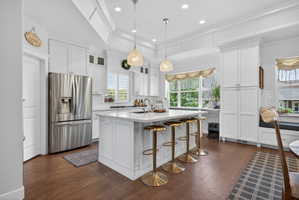 White kitchen featuring a central island with seating, stainless steel appliances, wood-finish flooring, white cabinetry, and a window seat with built-in storage