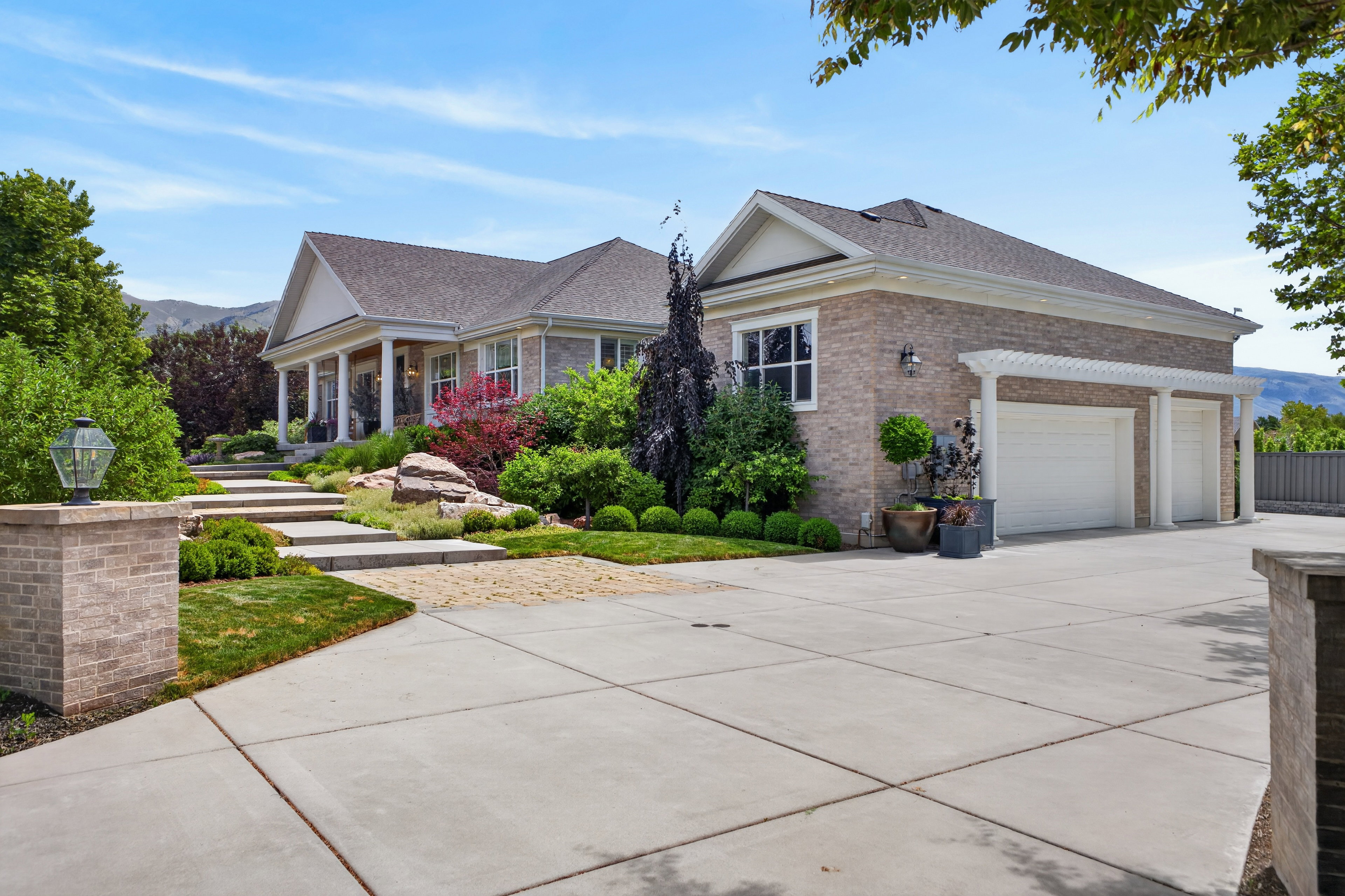 Spacious concrete driveway leading to a three-car garage with white doors and pergola detailing
