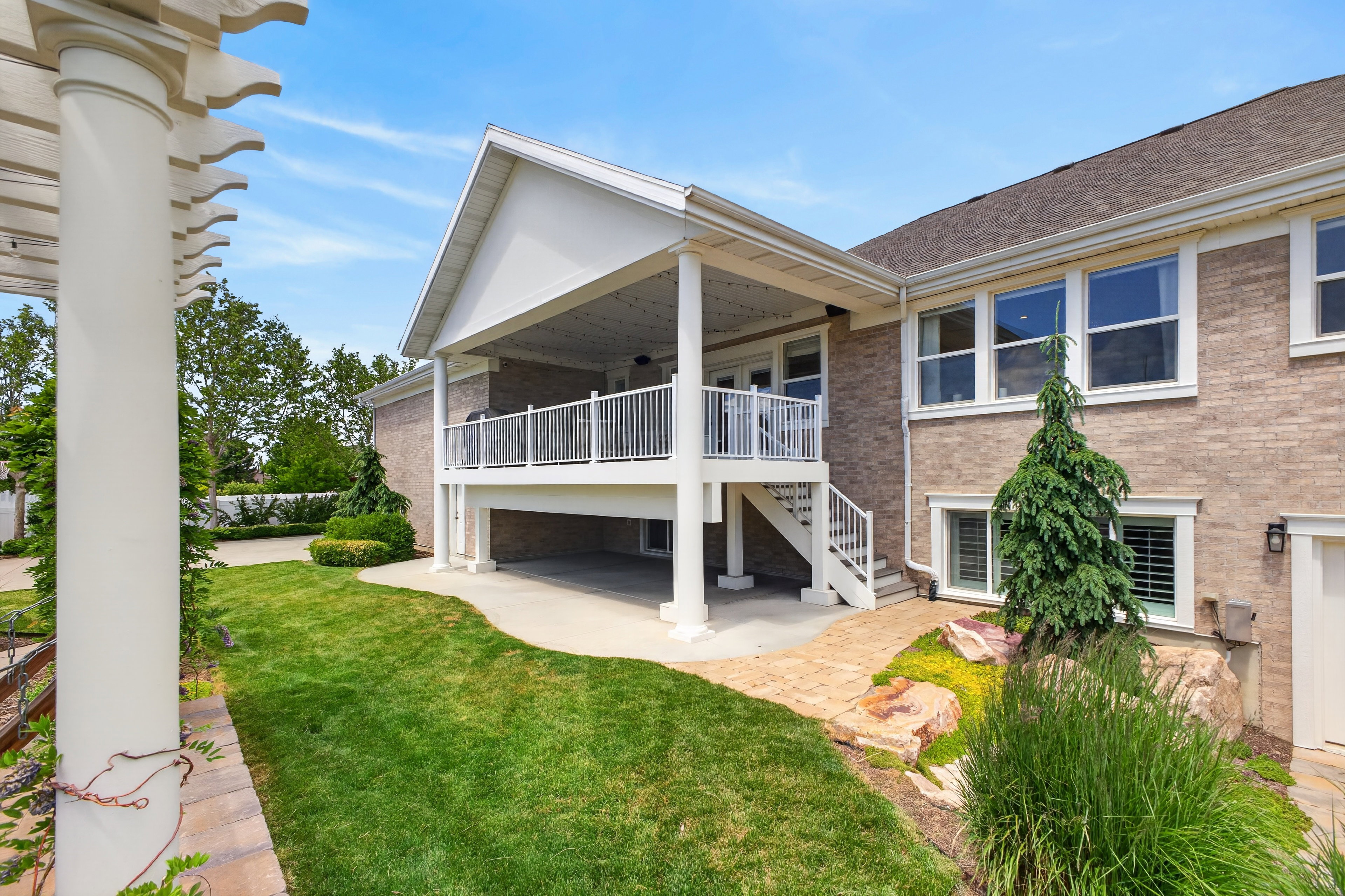 Brick exterior featuring a covered upper-level deck with white railing, a covered lower-level patio, and a manicured lawn
