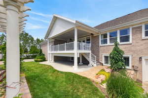Brick exterior featuring a covered upper-level deck with white railing, a covered lower-level patio, and a manicured lawn