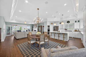 Open-concept living space featuring wood-finish flooring, a tray ceiling with recessed lighting, and a white kitchen with a large island