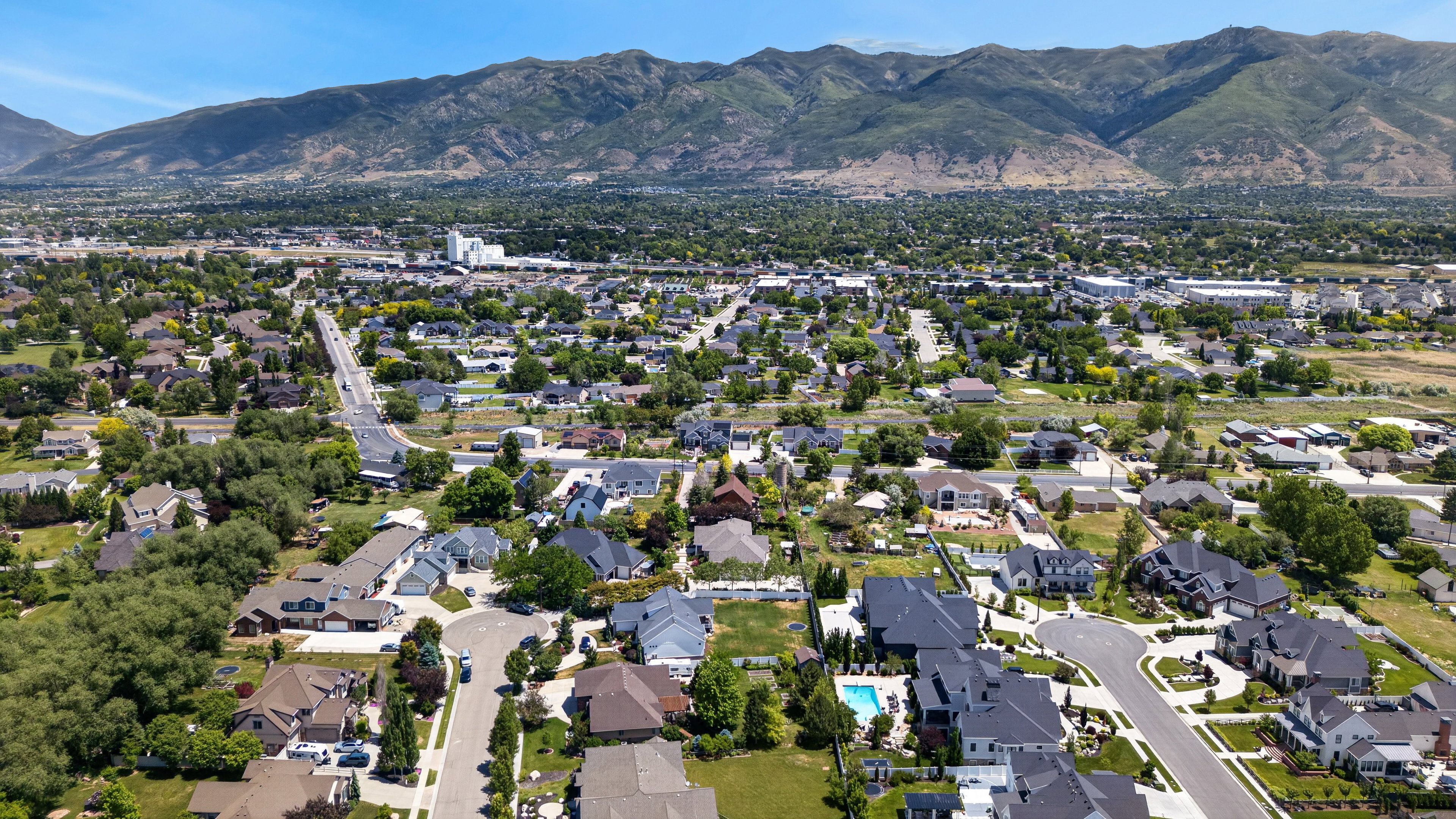 Expansive residential area featuring a diverse collection of homes, mature tree coverage, paved roads, and mountain backdrops