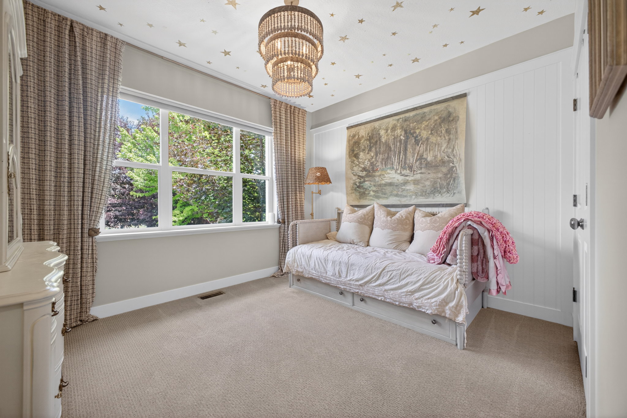 Bright room featuring a large multi-pane window, neutral-toned carpeting, white wainscoting, and a tiered chandelier