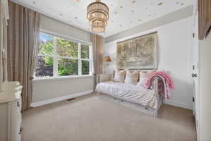 Bright room featuring a large multi-pane window, neutral-toned carpeting, white wainscoting, and a tiered chandelier