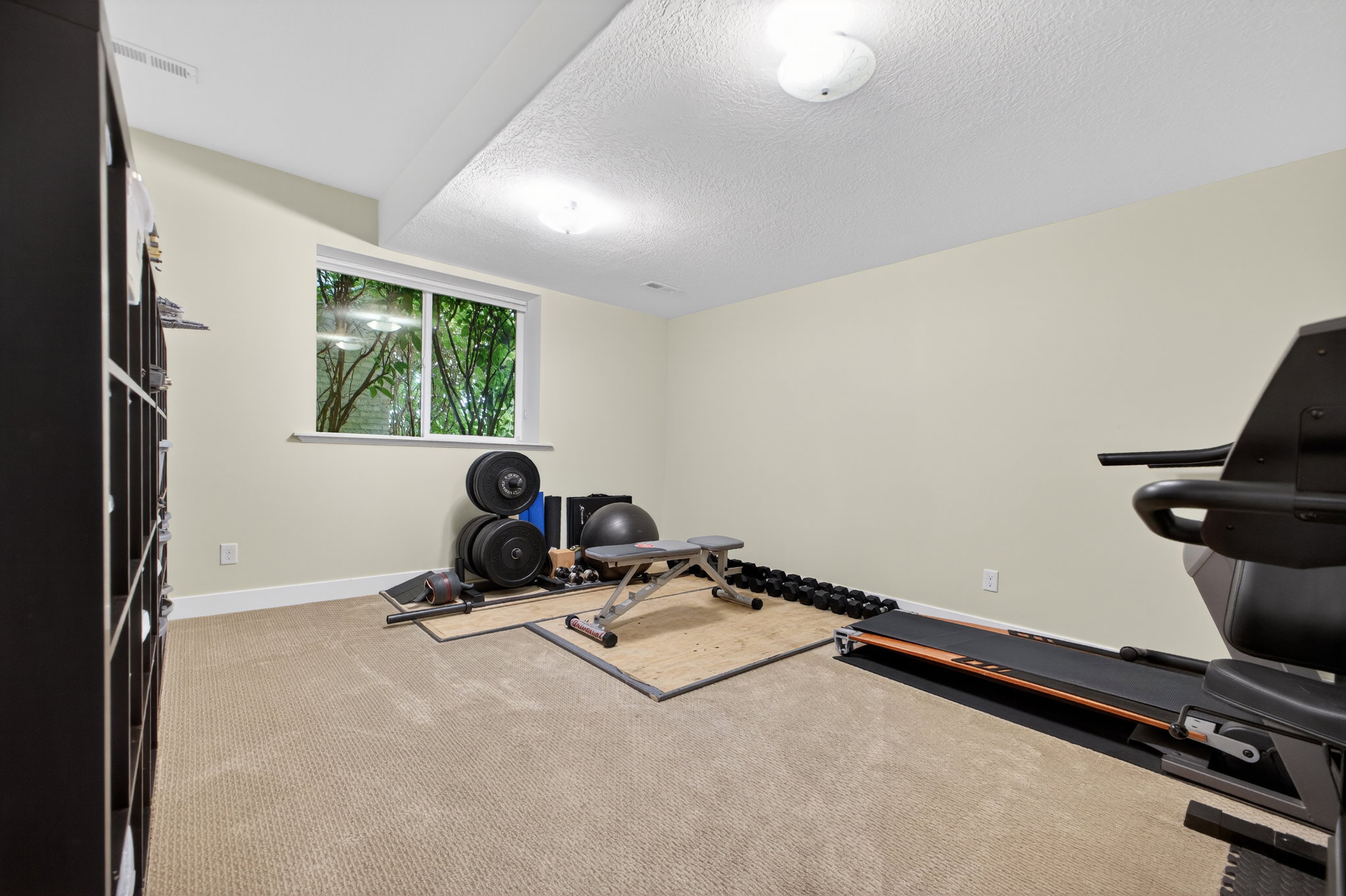 Carpeted room featuring a white-trimmed window, light-colored walls, recessed ceiling lighting, and a built-in shelving unit