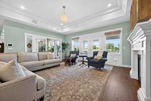 Spacious living area featuring a coffered ceiling with a central chandelier, wood-finish flooring, a white-mantled fireplace, and multiple French doors and windows