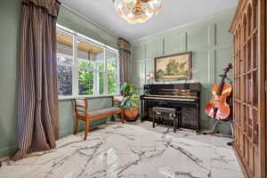 Room featuring large windows, a decorative chandelier, wainscoting paneling, and polished marble-look flooring