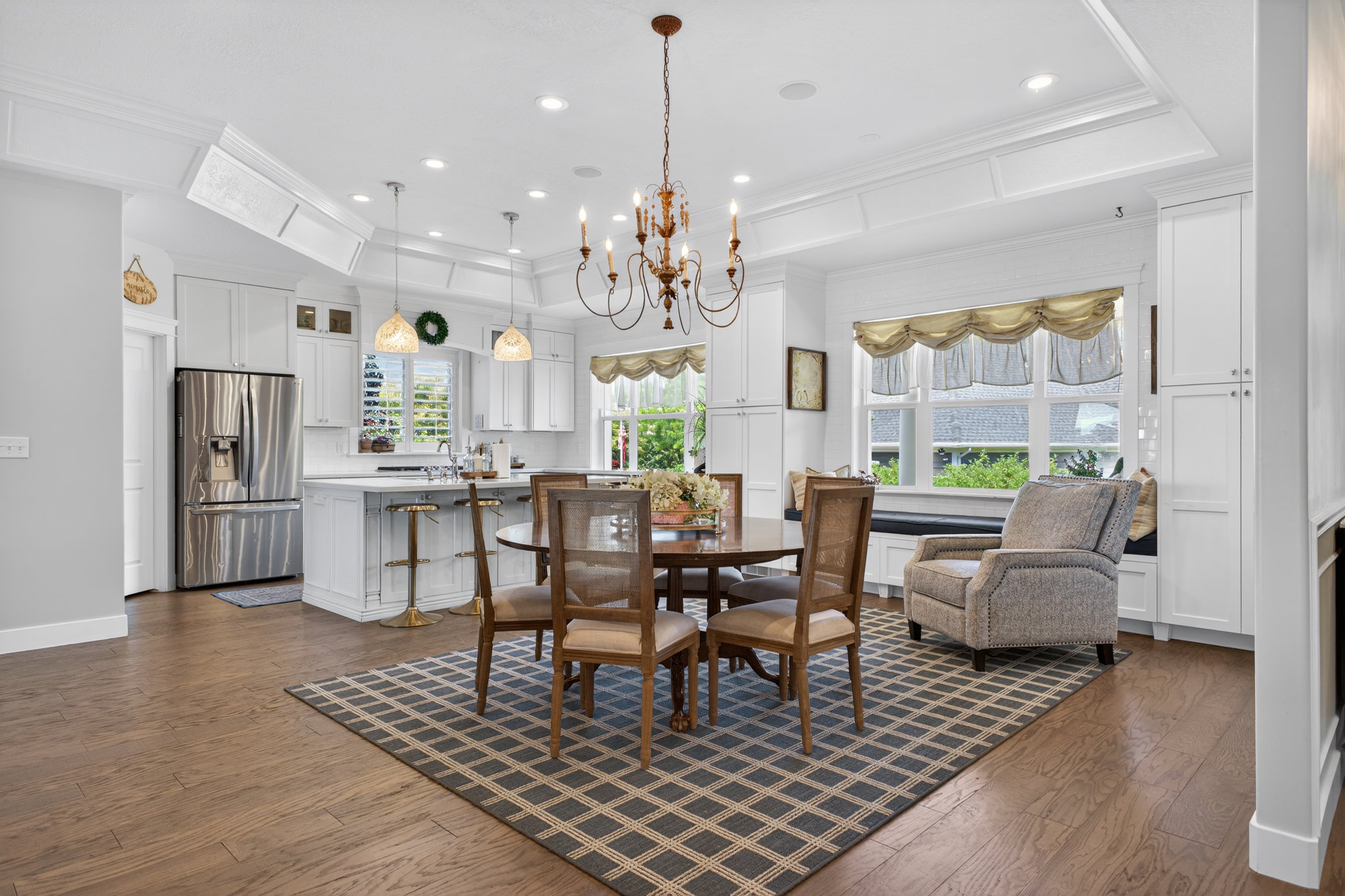 Bright kitchen and dining area featuring wood-finish flooring, white cabinetry, stainless steel appliances, and a coffered ceiling