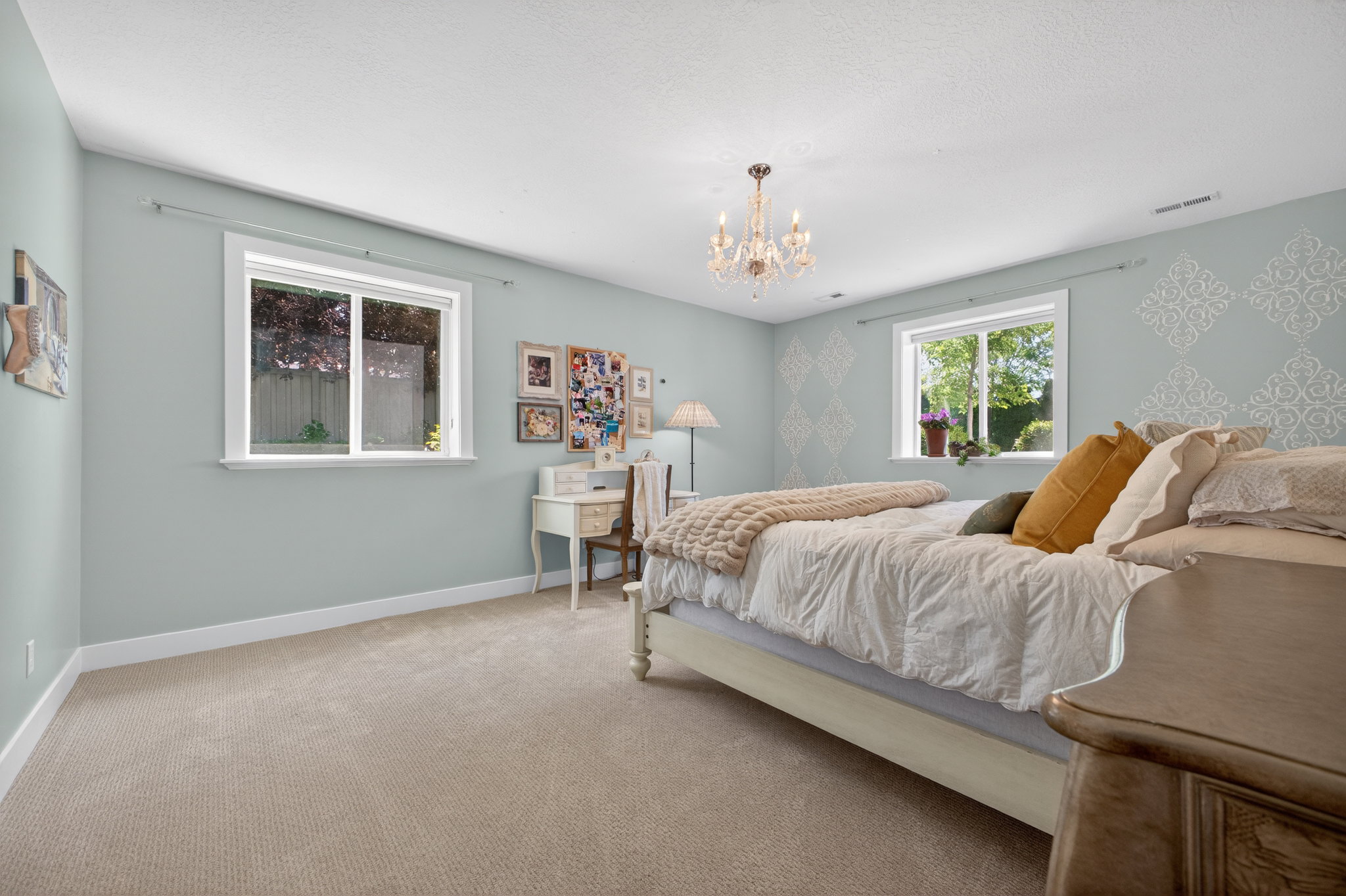 Room featuring neutral-toned carpeting, light blue walls with decorative stenciling, white trim, and two windows