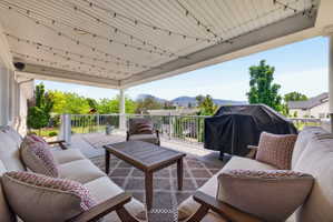 Spacious covered deck featuring a white railing, a patterned outdoor rug, and string lighting